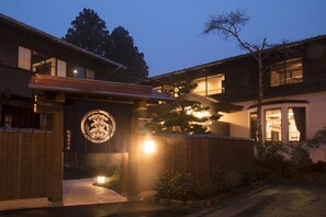 Een traditioneel Japans gebouw met een houten gevel, een groot verlicht logo en een verzorgde tuin met een opvallende boom.