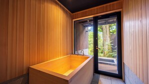 Un baño moderno con paredes de madera, una bañera grande y una puerta de vidrio corredera que da a un espacio exterior.