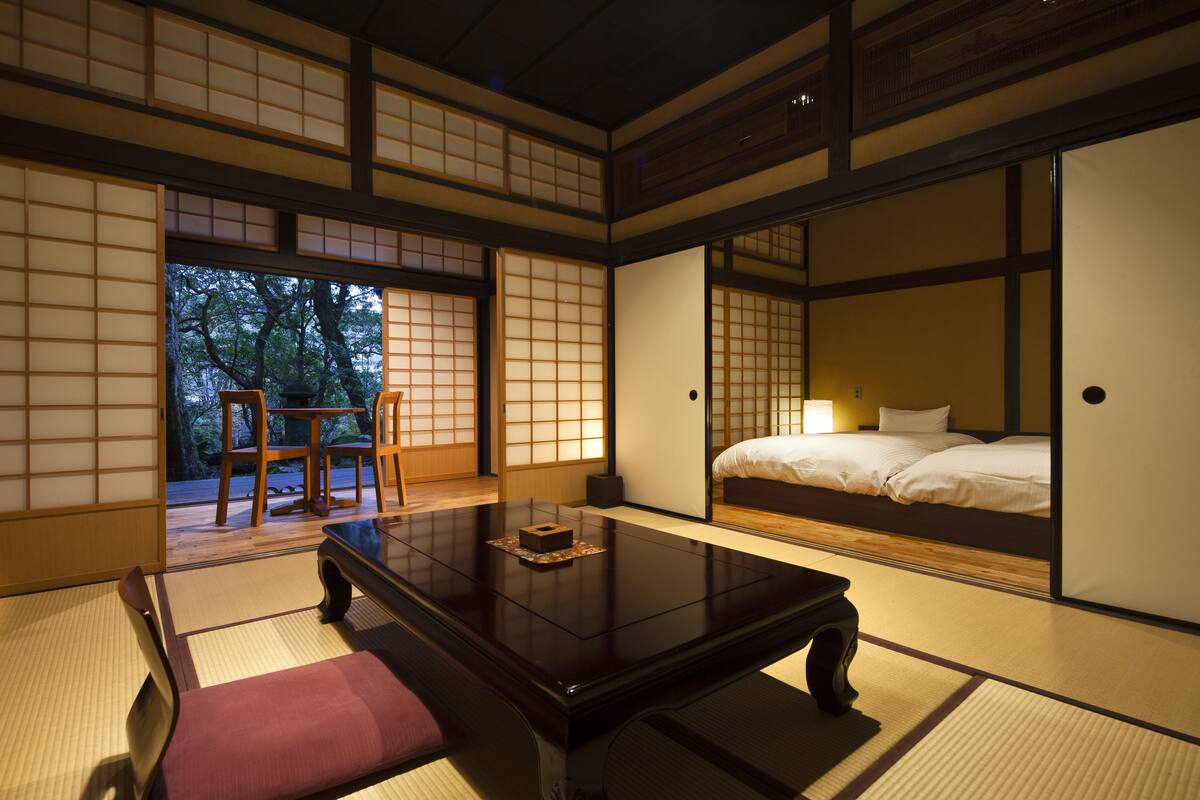 A traditional Japanese room with tatami flooring, a low wooden table, a bed with white bedding, and sliding doors.