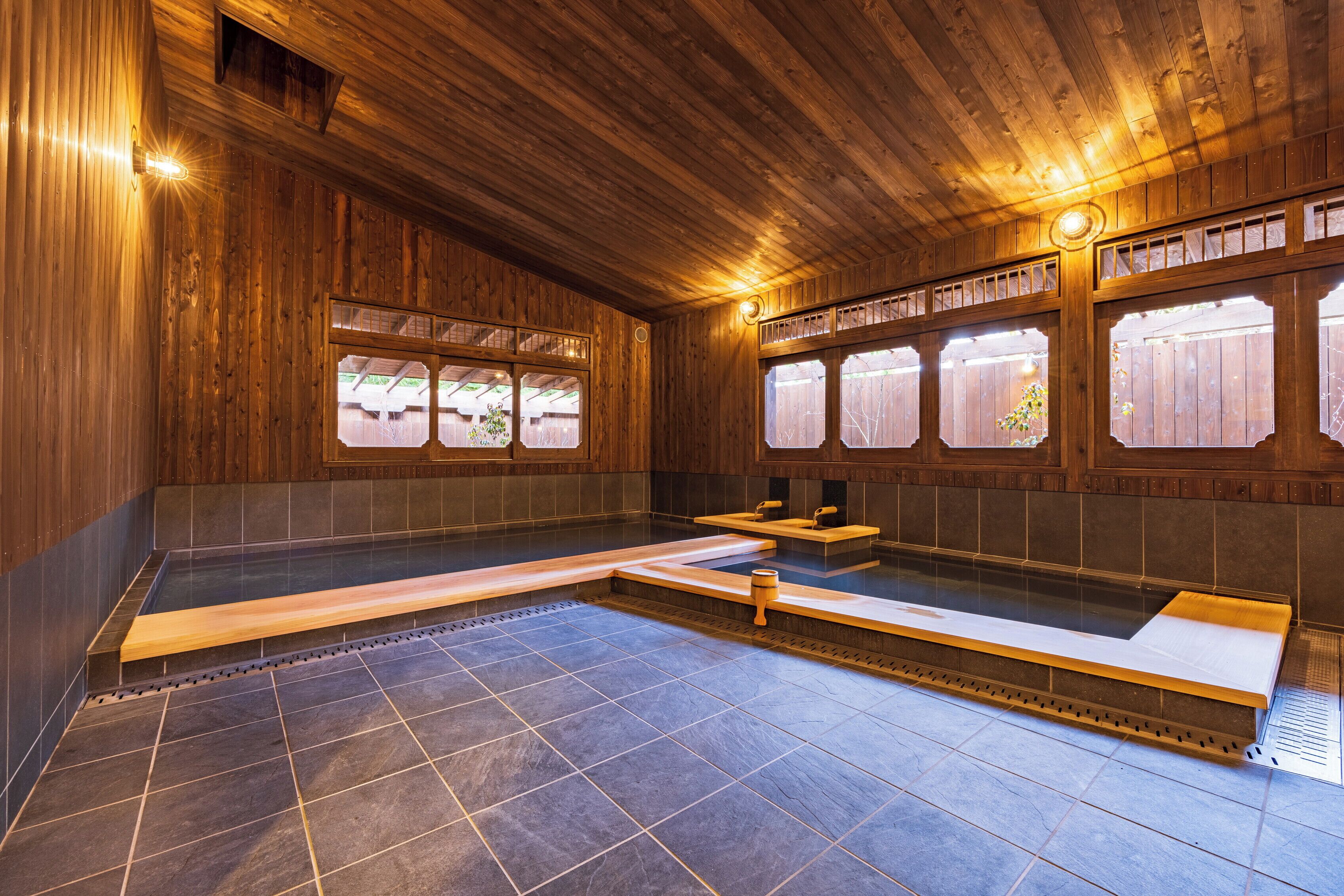 A wooden interior with a hot tub, benches, and windows.