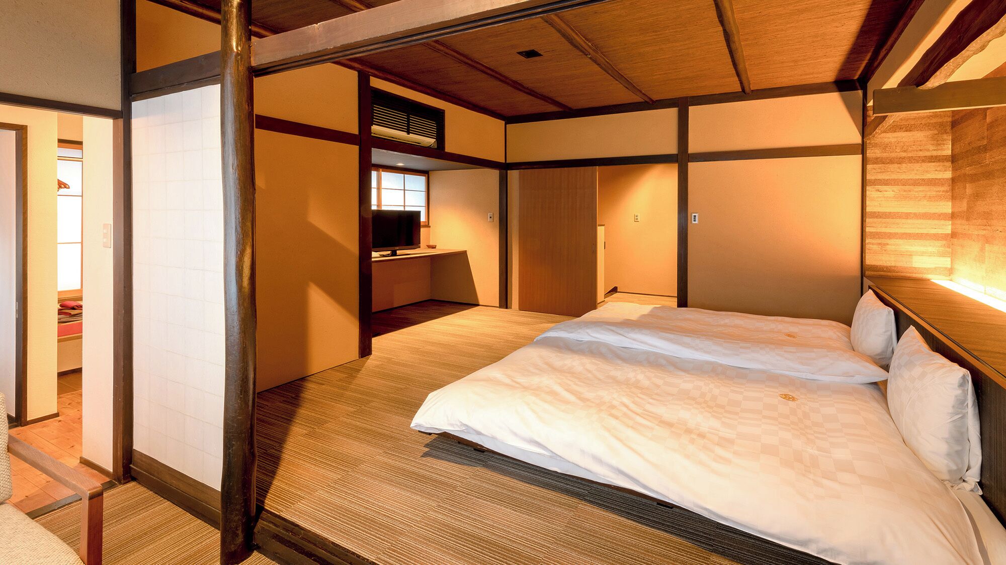 A traditional Japanese-style room with tatami flooring, a low wooden bed, a sliding door, and a small desk with a television.