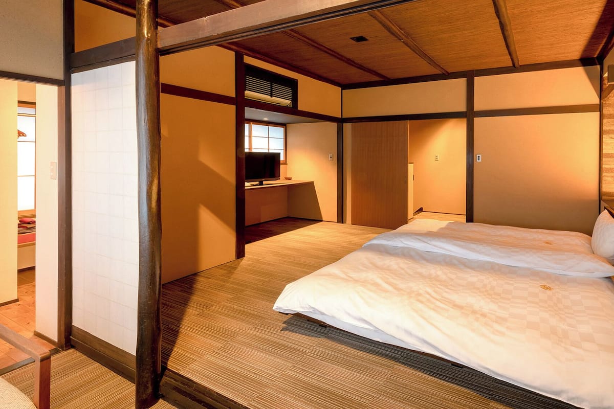 A traditional Japanese-style room with tatami flooring, a low wooden bed, a sliding door, and a small desk with a television.