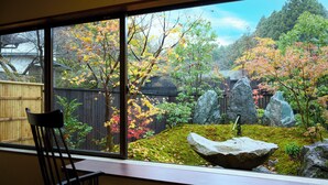 Vista de un jardín con rocas, árboles y una valla de madera a través de una ventana.