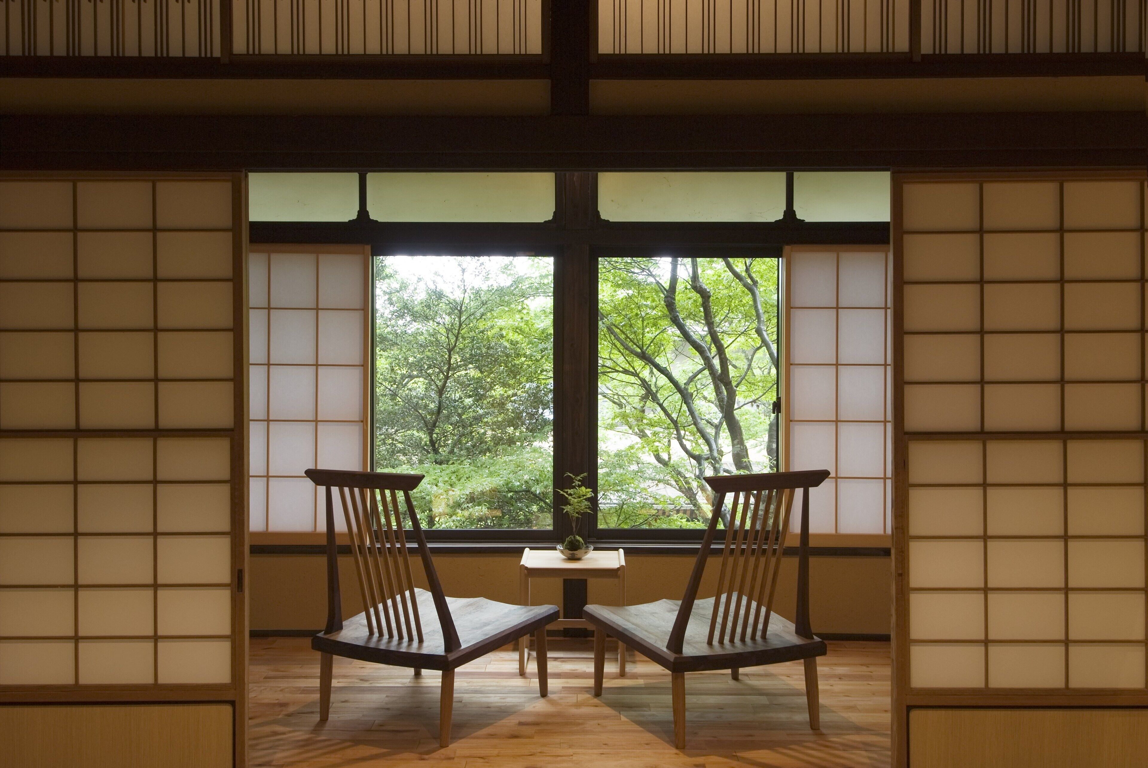 A traditional Japanese room with tatami flooring, a low table with a small plant, and two wooden chairs facing a window with a view of trees.