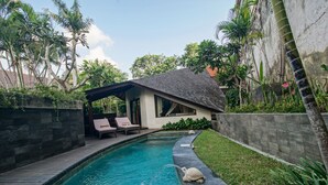 A swimming pool with a wooden deck, a covered seating area, and lush greenery. - Baliana Villa Umalas (Kerobokan)