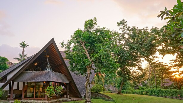A modern building with a triangular roof and large windows, surrounded by lush greenery and a well-maintained lawn. - Baliana Villa Umalas (Kerobokan)