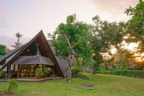 Um edifício moderno com telhado triangular e janelas amplas, rodeado por vegetação exuberante e um gramado bem cuidado.