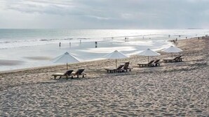 A beach with sun loungers and umbrellas, a sandy shore, and the ocean in the background. - Baliana Villa Umalas (Kerobokan)