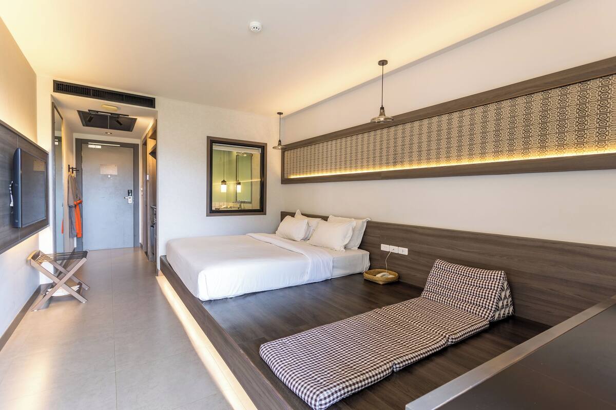A modern hotel room with a large bed, a sofa, a TV, and a mirror.