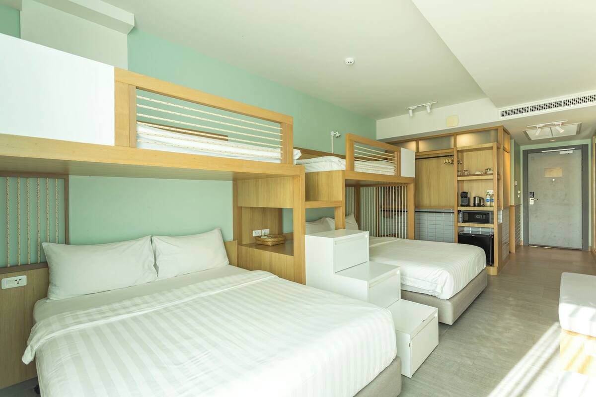A modern hotel room with bunk beds, a kitchenette, and a bathroom.