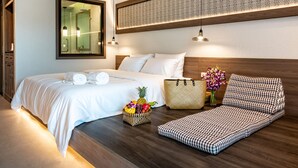 Una habitación de hotel con una cama grande, una cama más pequeña, un sofá, un espejo, una pared con diseño decorativo y una cesta de frutas.