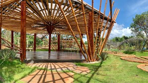 Un pabellón de bambú con una plataforma central, rodeado por un jardín con jardineras elevadas y una valla.