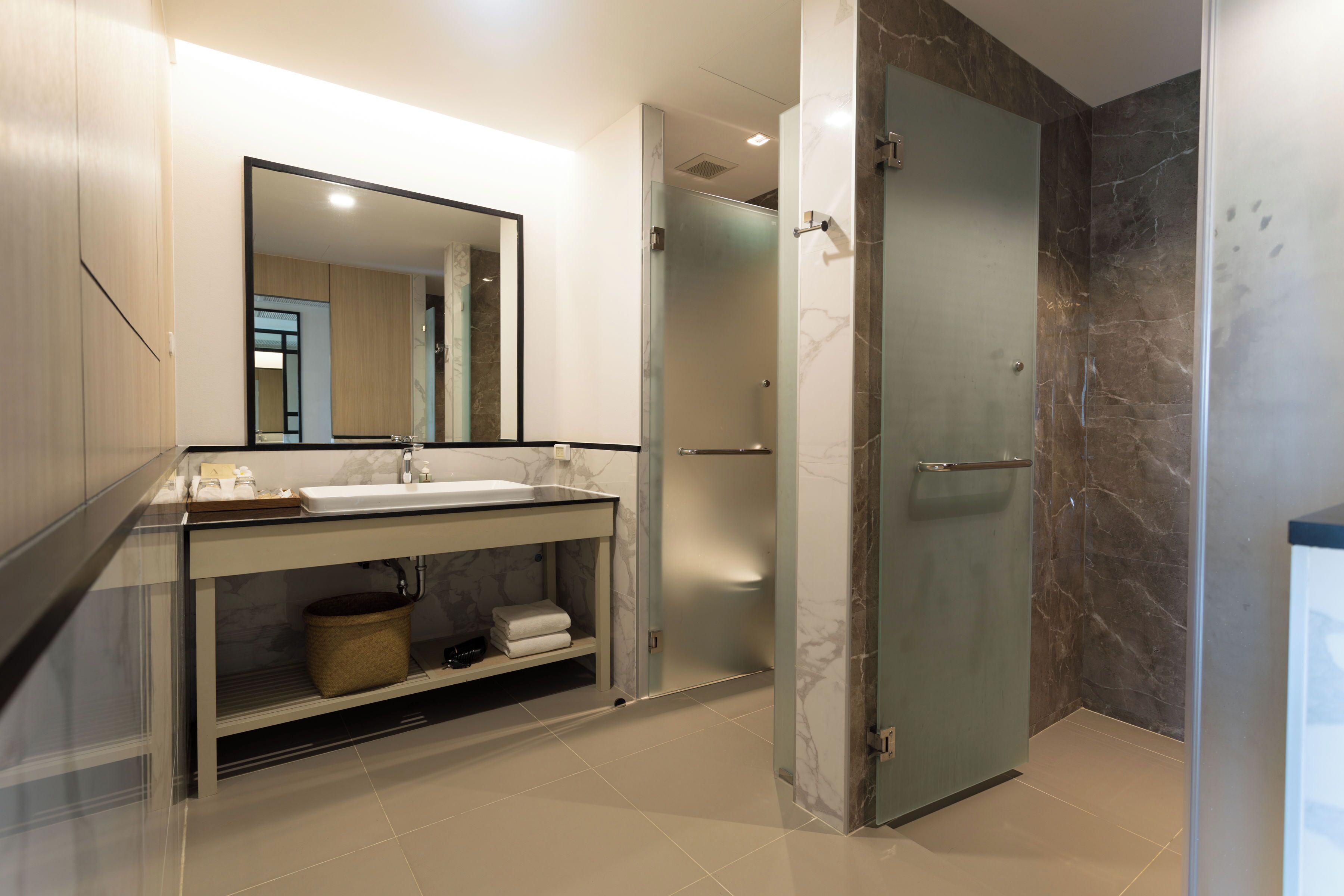 Un baño moderno con cabina de ducha de vidrio, suelo de baldosas de mármol y un espejo grande sobre el lavamanos.