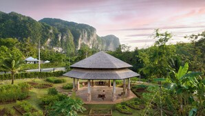 Un quiosco con techo de tejas rodeado de un jardín con diversas plantas y vistas a un paisaje montañoso.