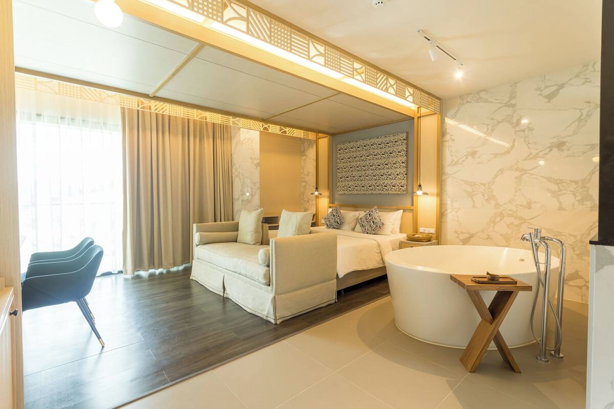 A modern hotel room with a large bathtub, a sofa, a chair, and a bed.