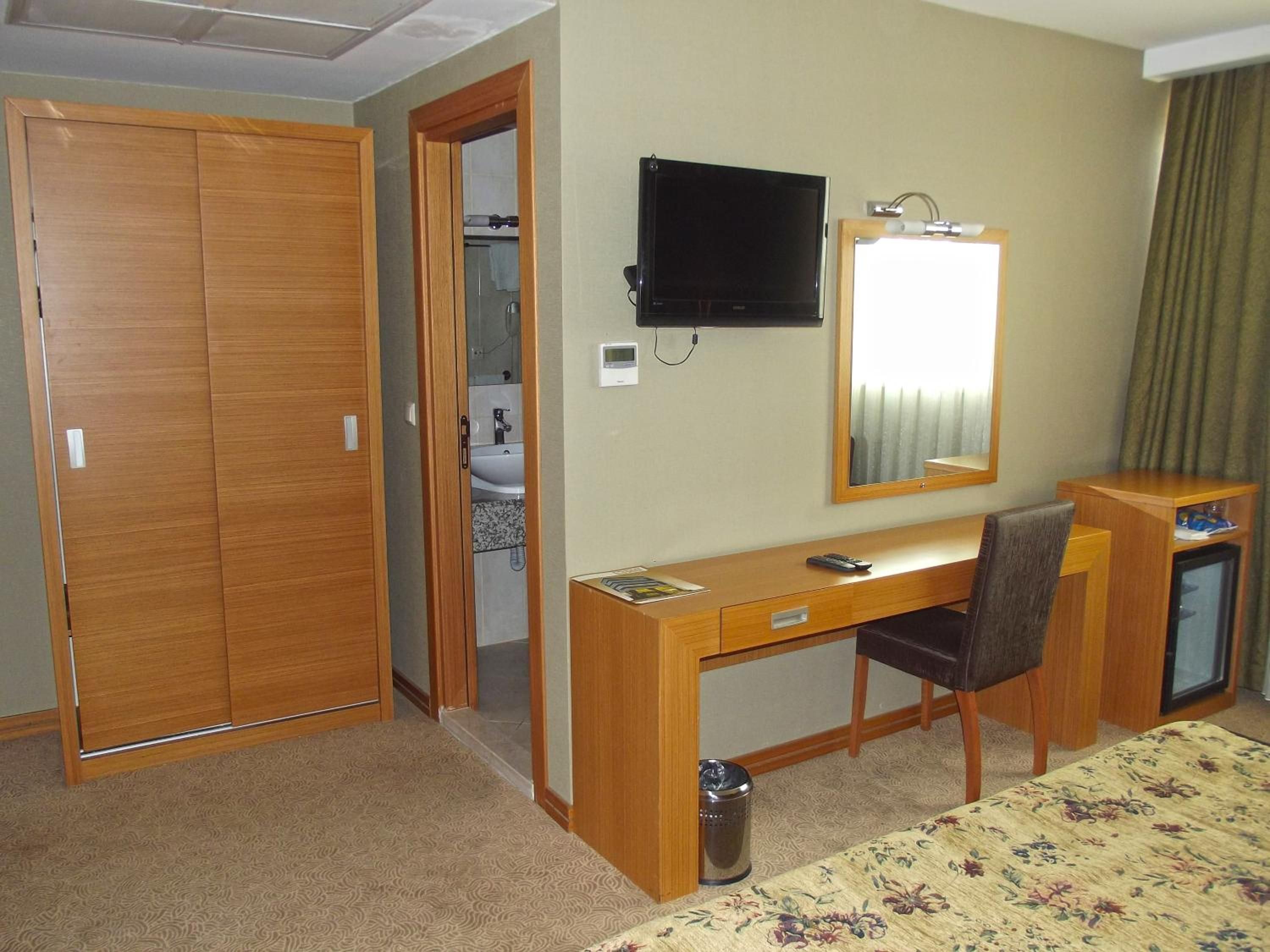 A hotel room with a wooden desk, a television, a mirror, a bed, and a bathroom visible through an open door.