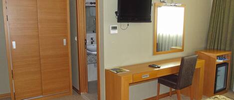 A hotel room with a wooden desk, a television, a mirror, a bed, and a bathroom visible through an open door.