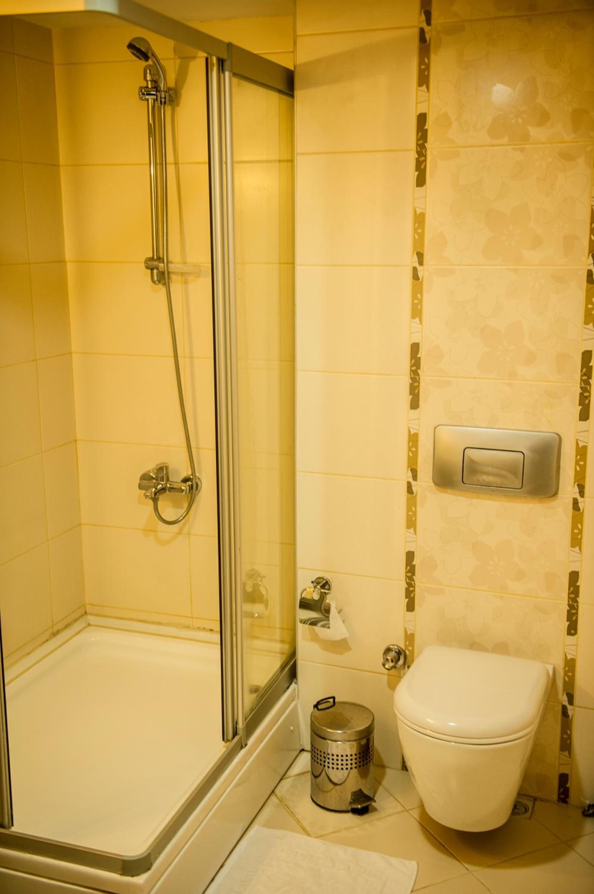 A bathroom with a glass-enclosed shower, a toilet, and a trash can.