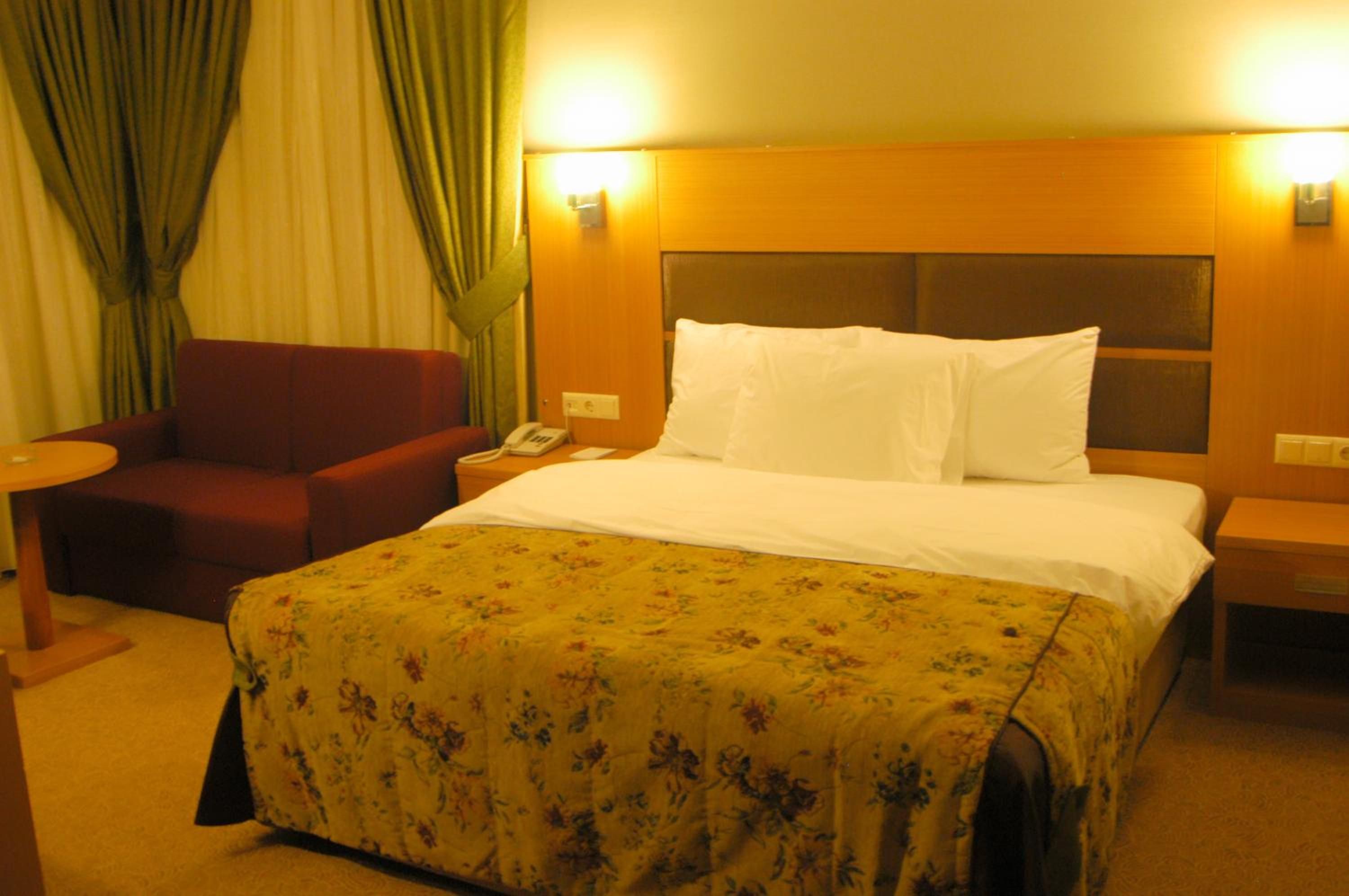 A hotel room with a bed, a chair, a bedside table, and a lamp.
