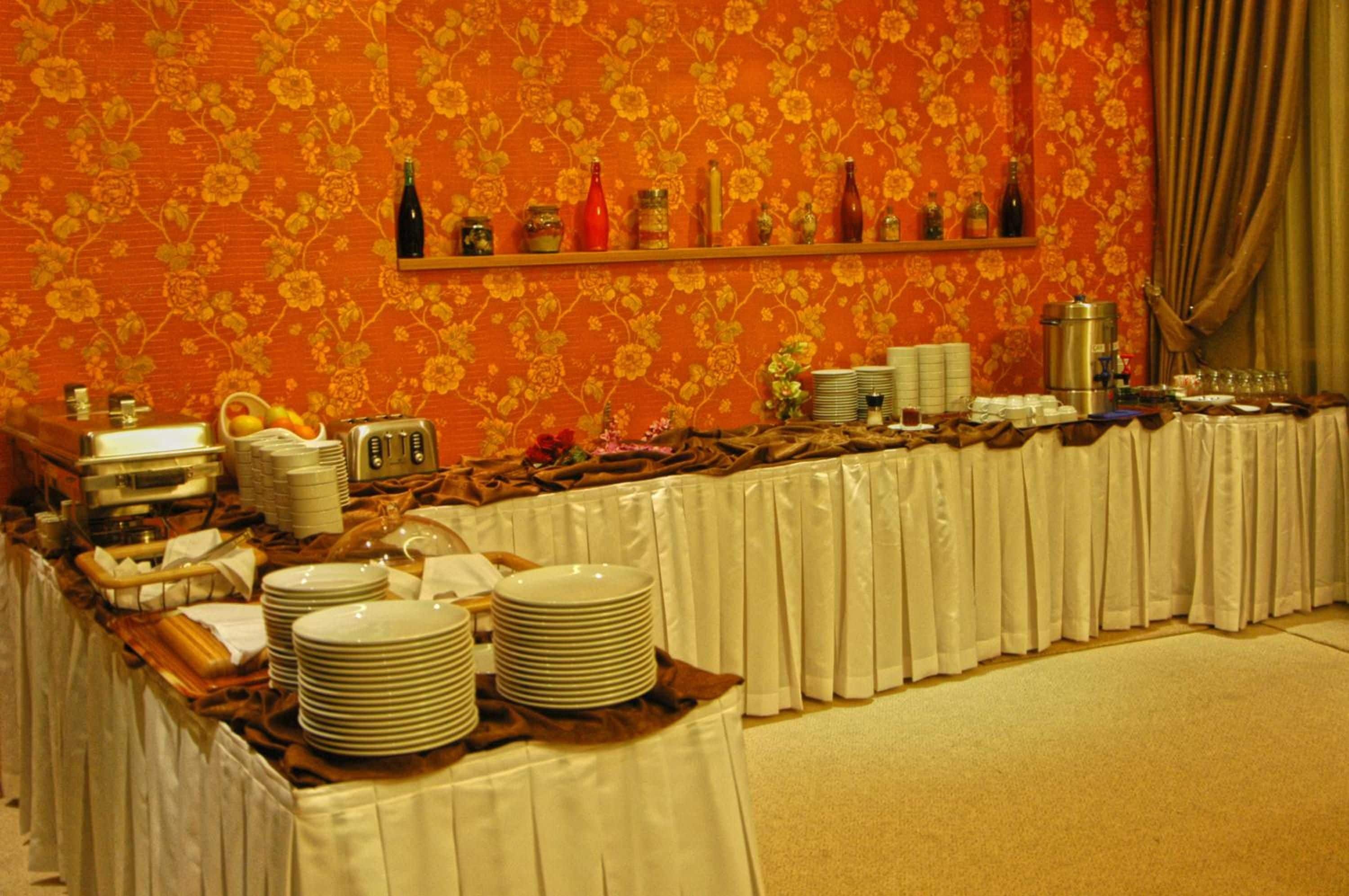 A buffet setup with a variety of dishes and beverages, a decorative wall, and a curtain.