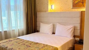 A hotel room with a bed, a nightstand, a lamp, and a floral painting on the wall. - Pinar Elite Hotel (Adana)