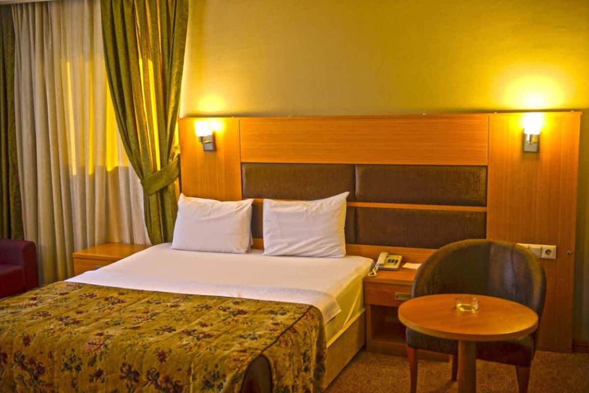 A hotel room with a bed, a bedside table with a lamp, a chair, and a small table.