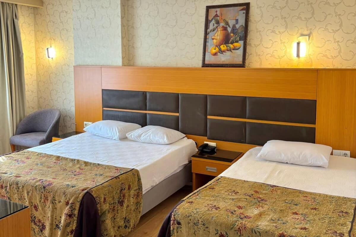 A hotel room with two beds, a desk, a chair, and a painting on the wall.