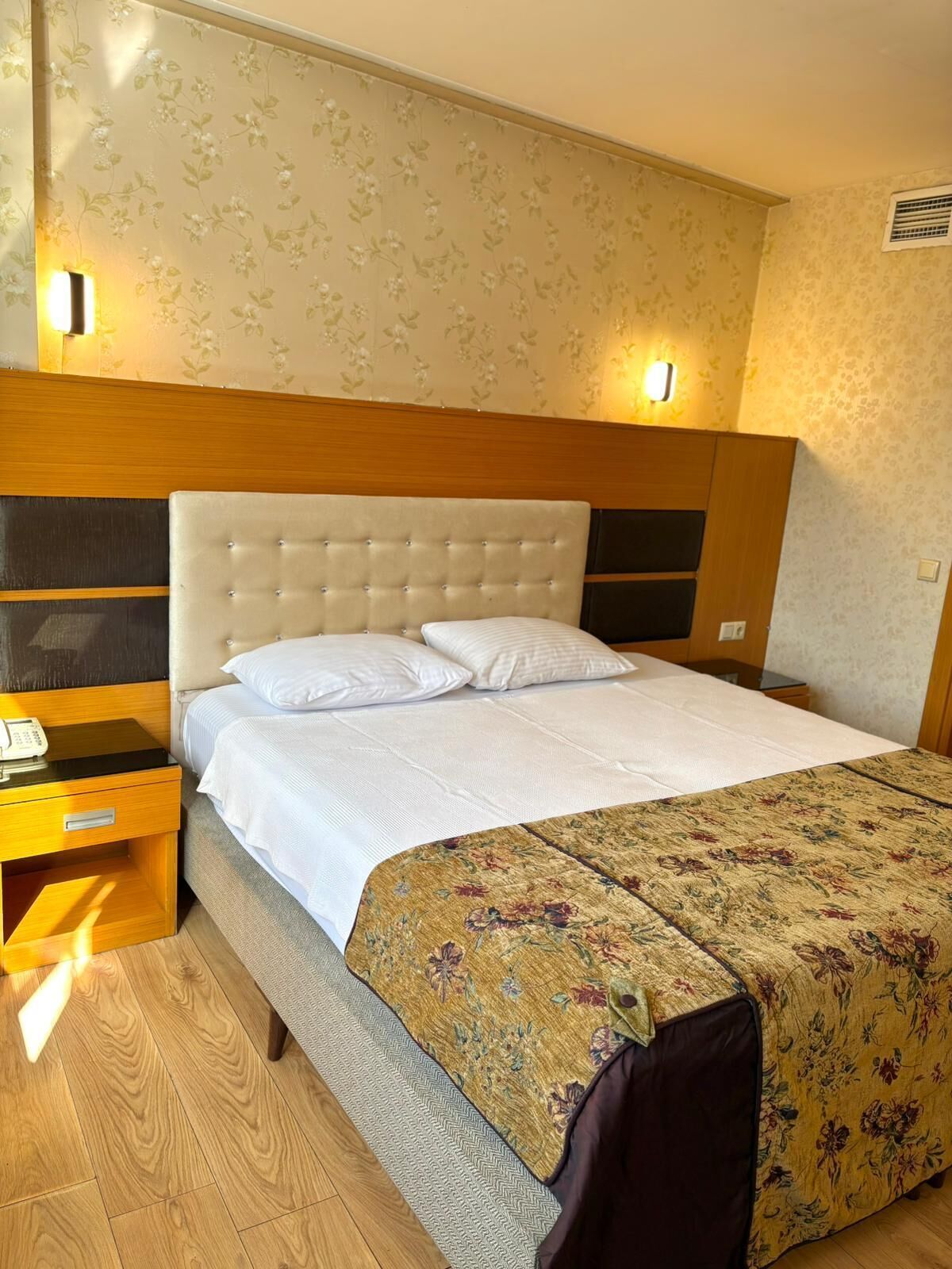 Habitació d'hotel amb un llit, una nit de nit de fusta i un edredó amb estampat floral.