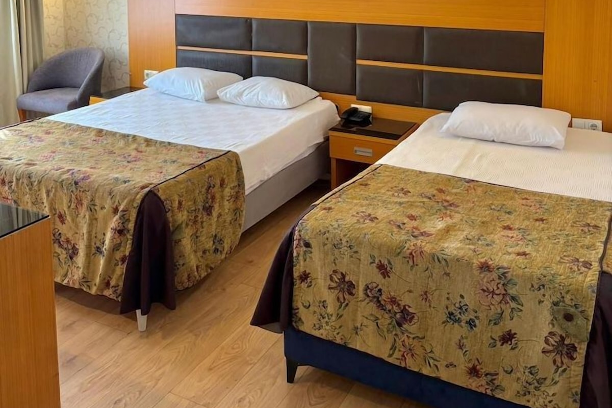 Habitación de hotel con dos camas, una silla, un escritorio y un cuadro en la pared.