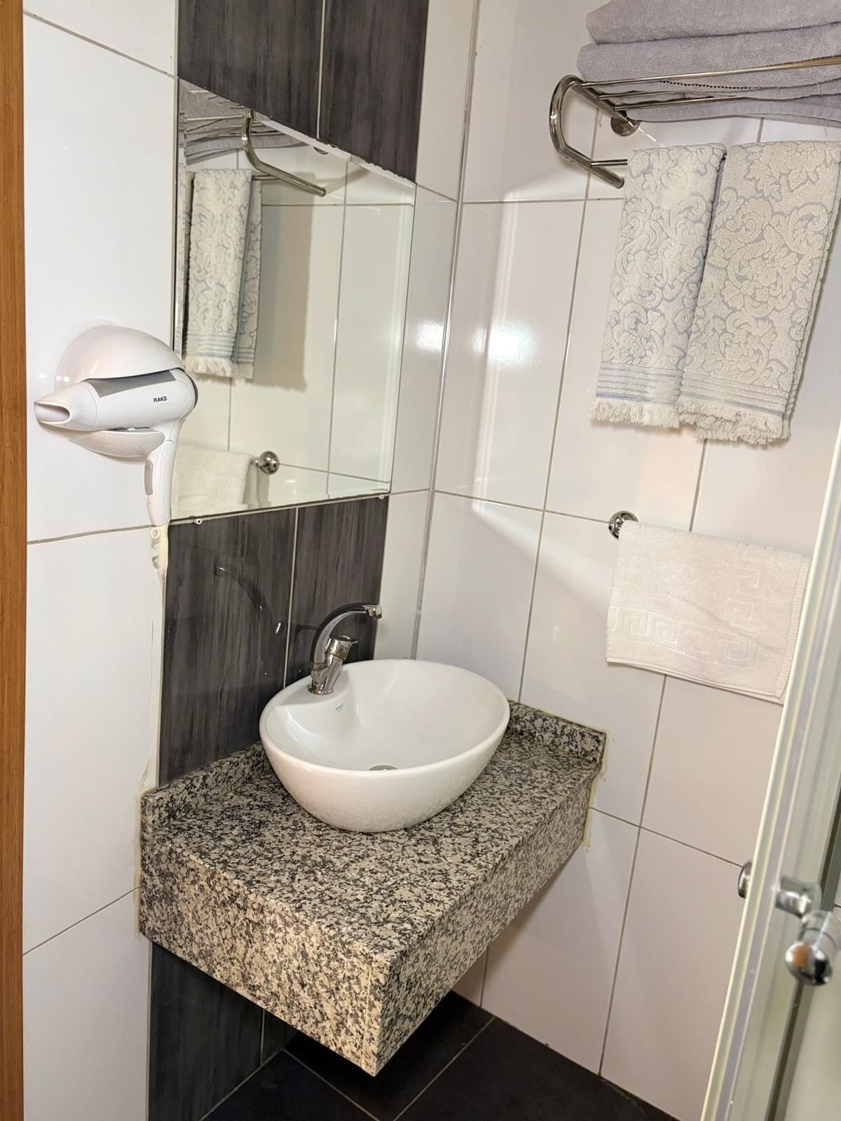 A bathroom with a white sink, granite countertop, dark tiles, a mirror, and a hairdryer.