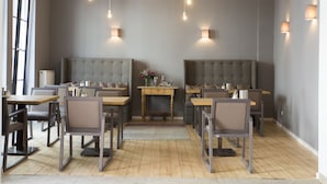 A dining area with multiple tables and chairs, a central seating area with a cushioned bench, and pendant lighting. - Cottage Rheingau Hotel (Walluf)