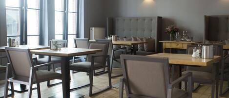Un comedor moderno con mesas y sillas de madera, ventanas amplias y una banqueta tapizada de gris.