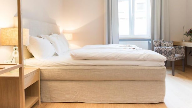 A modern bedroom with a bed, bedside table, lamp, chair, and a view of the outside. - Cottage Rheingau Hotel (Walluf)