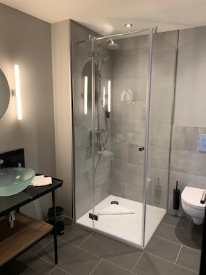 Un baño moderno con ducha de vidrio, lavamanos de vidrio y un inodoro.
