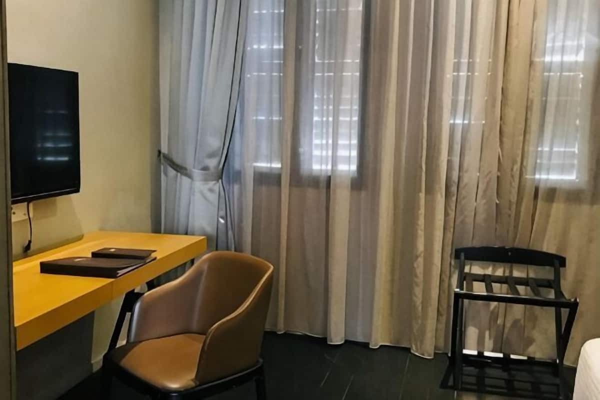 A hotel room with a bed, a desk with a chair, a television, and a window with curtains.