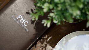 A brown leather-bound book with "PHC" and "PENANG HOTEL COLLECTION" embossed on it, placed on a wooden surface next to a white plate and a glass.