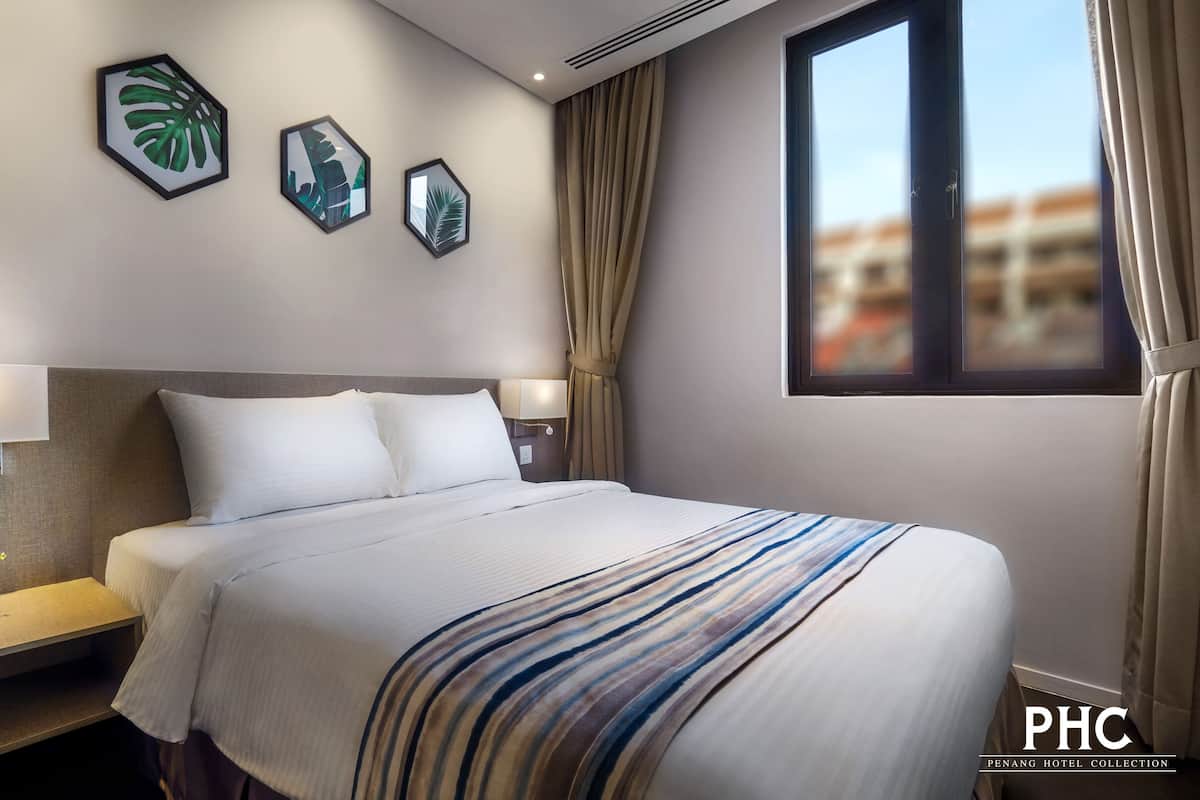 A hotel room with a large bed, a nightstand with a lamp, a potted plant, and framed artwork on the wall.