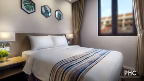 A hotel room with a large bed, a nightstand with a lamp, a potted plant, and framed artwork on the wall.