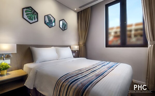A hotel room with a large bed, a nightstand with a lamp, a potted plant, and framed artwork on the wall.