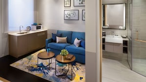 A modern hotel room with a kitchenette, a blue sofa, a small coffee table, and a shower area.