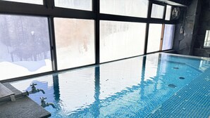 Una piscina interior con agua cristalina, escalones de piedra para entrar y amplias ventanas que dejan entrar luz natural.