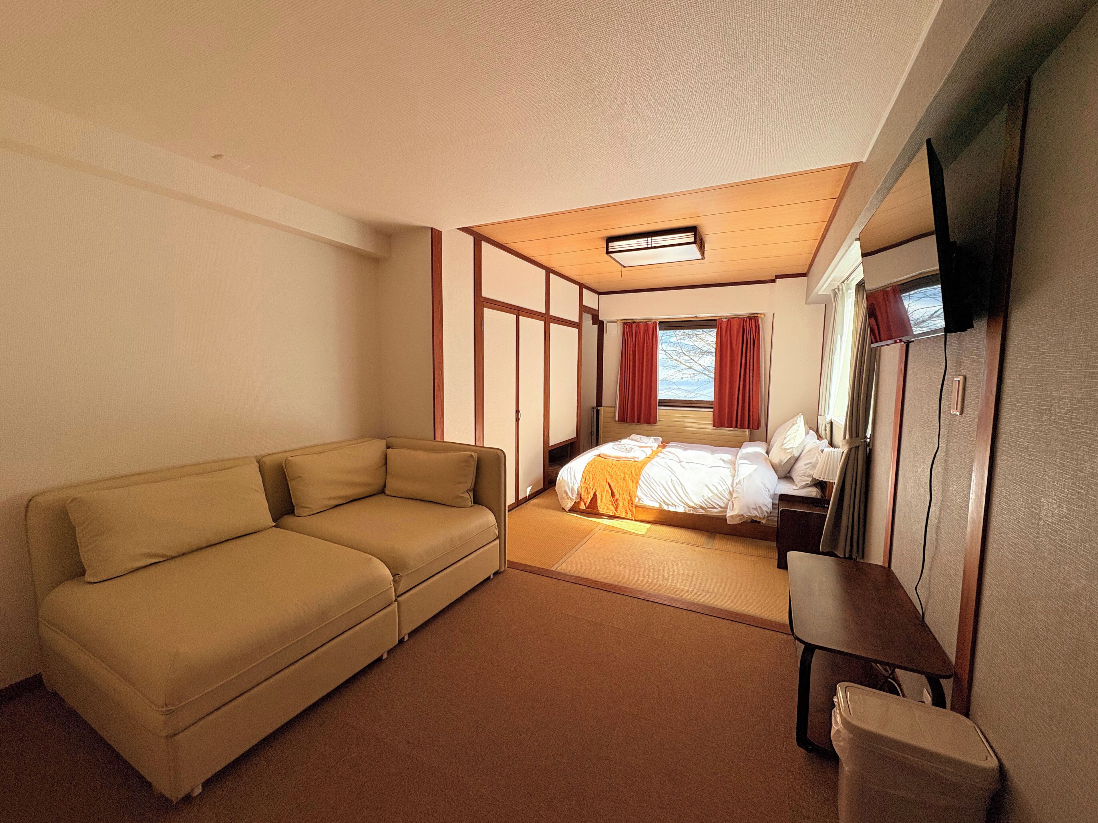 A compact hotel room with a sofa, a bed, a small table, and a TV.