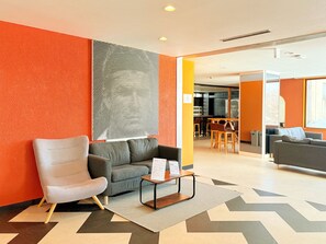 Una hall moderna con un divano grigio, una poltrona bianca e un tavolino con i menu.