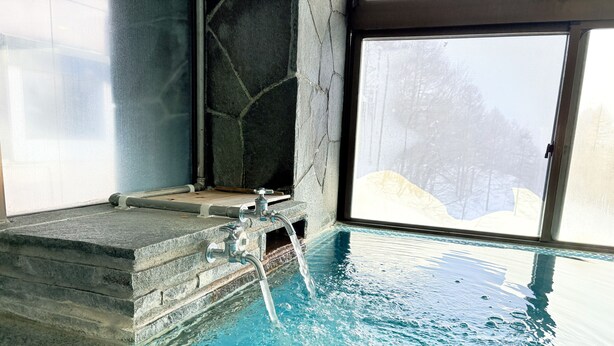 Piscina interior con suelo de piedra, agua cristalina, pared de piedra y ventana con vistas a árboles.