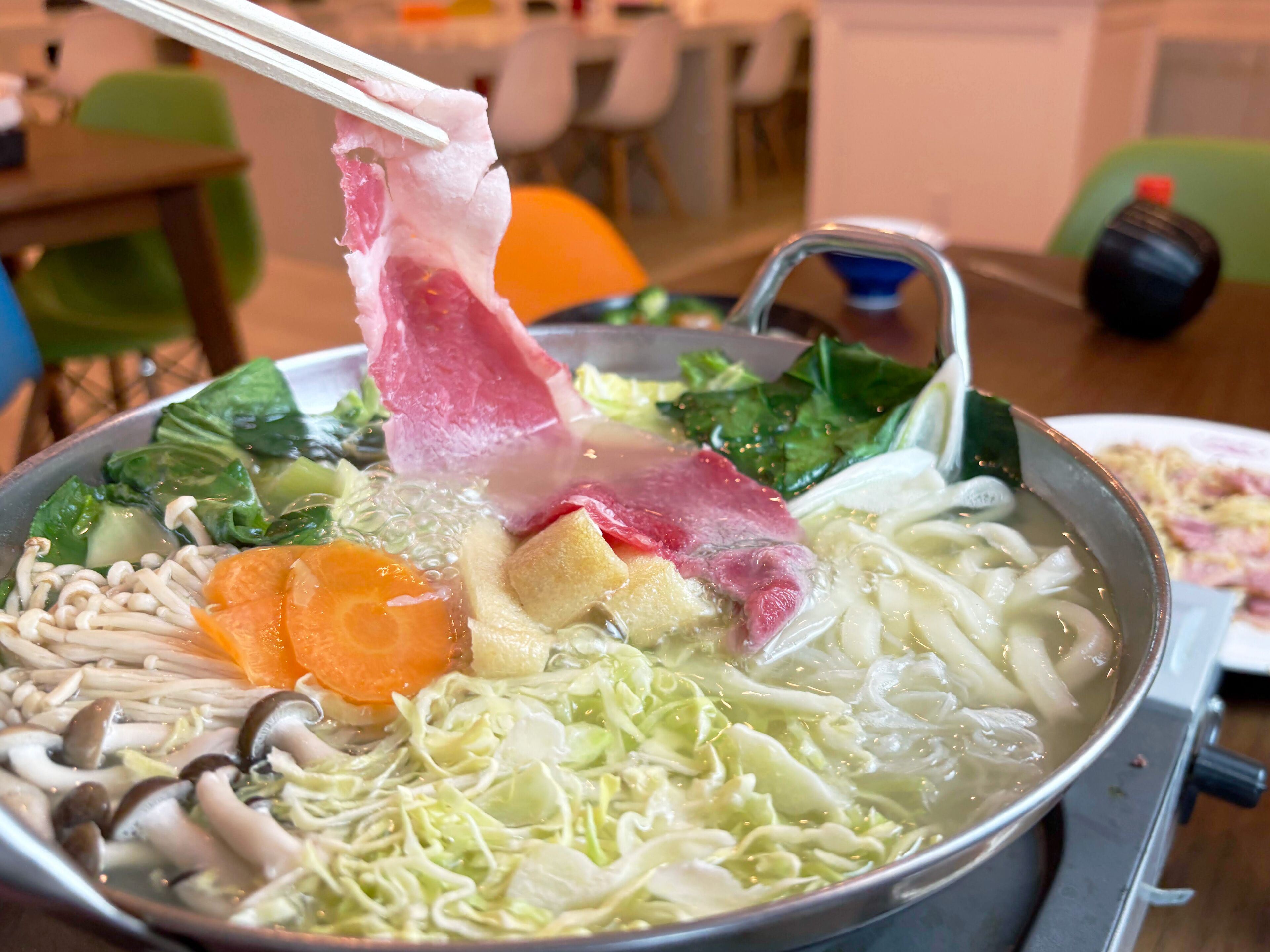 Una olla de sopa con varios ingredientes como champiñones, zanahorias y verduras de hoja.