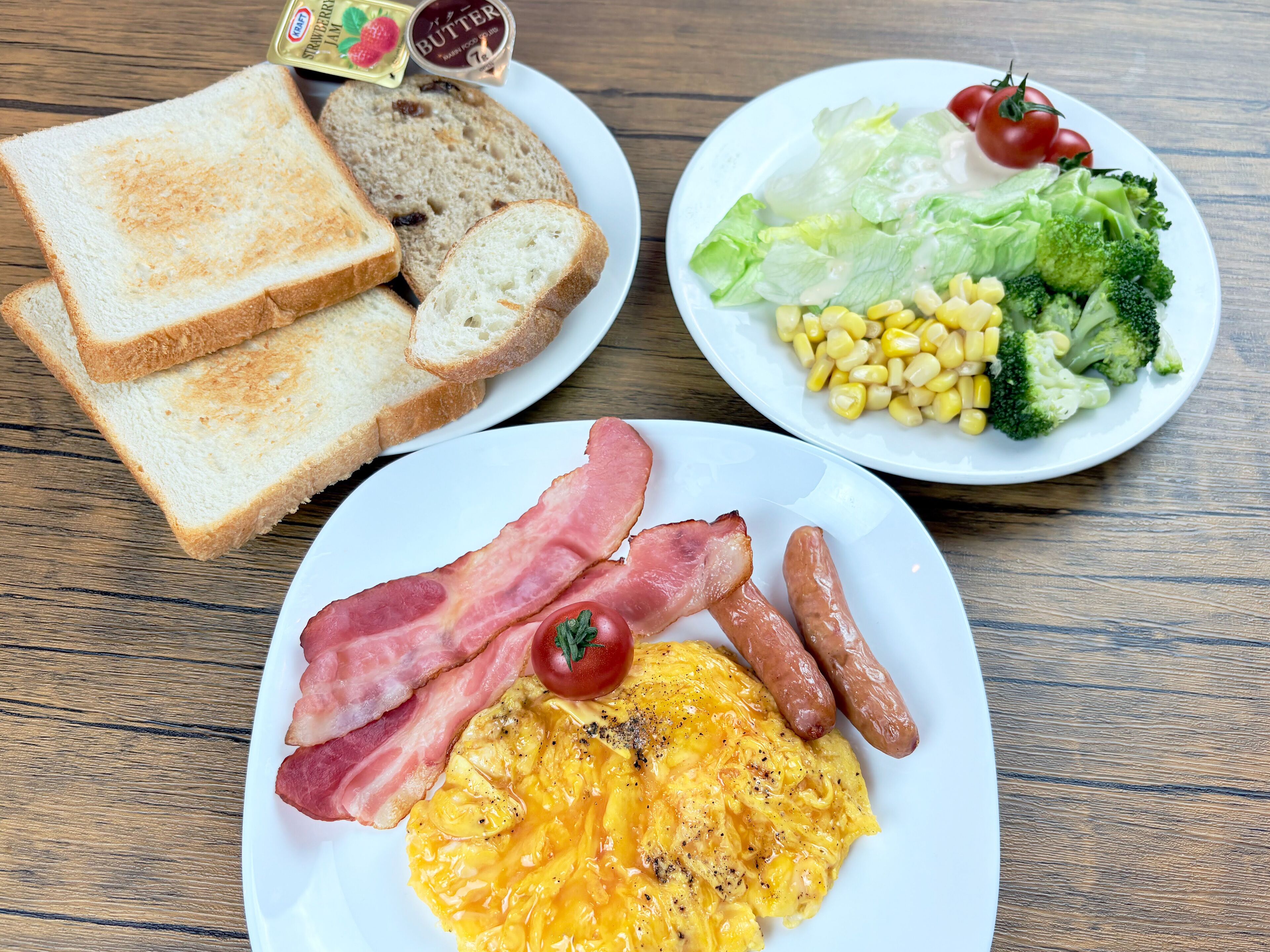 A breakfast plate with toast, butter, bacon, sausages, and scrambled eggs.
