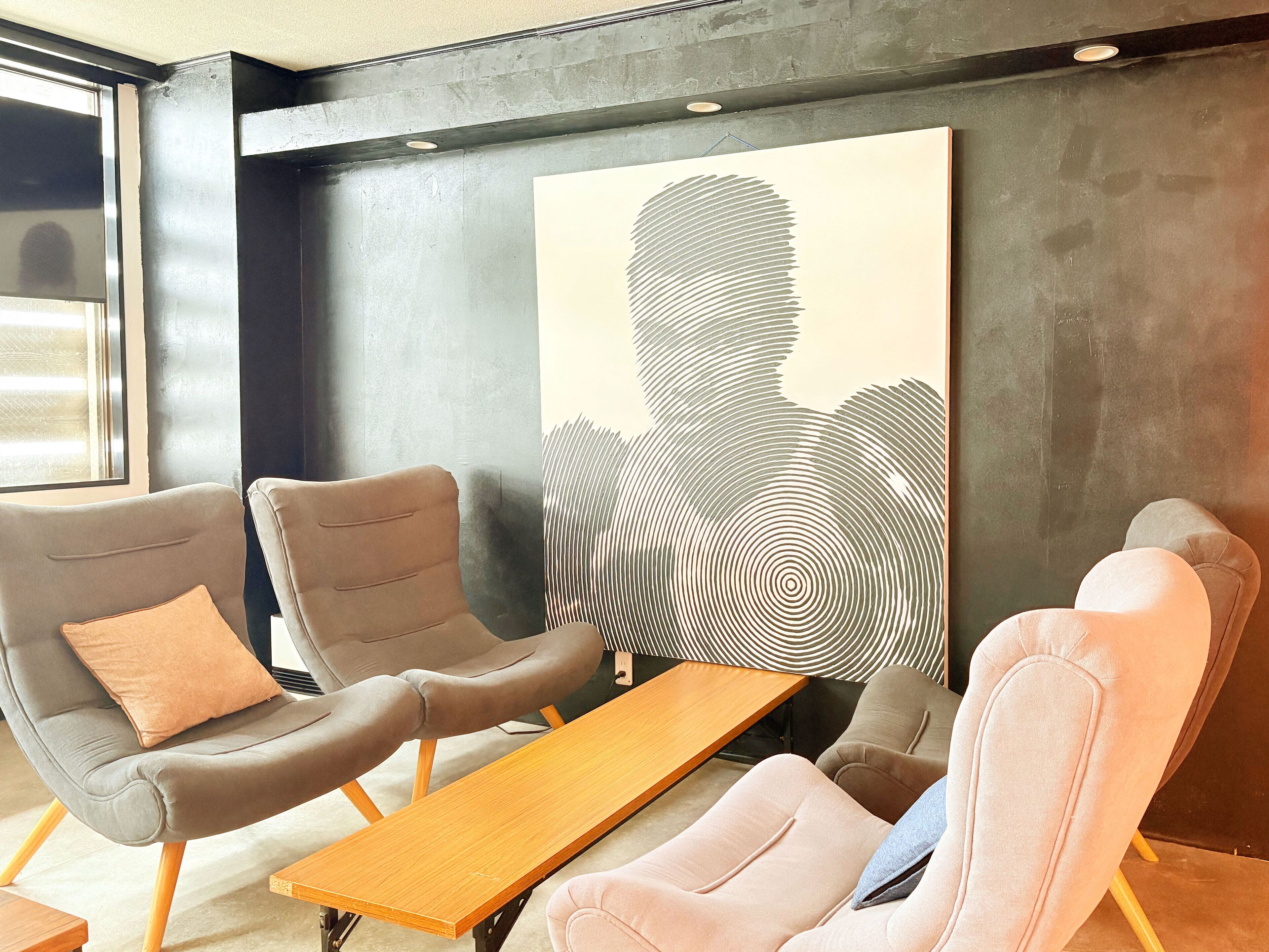 A modern waiting area with leather chairs, a wooden table, and a large abstract painting on the wall.