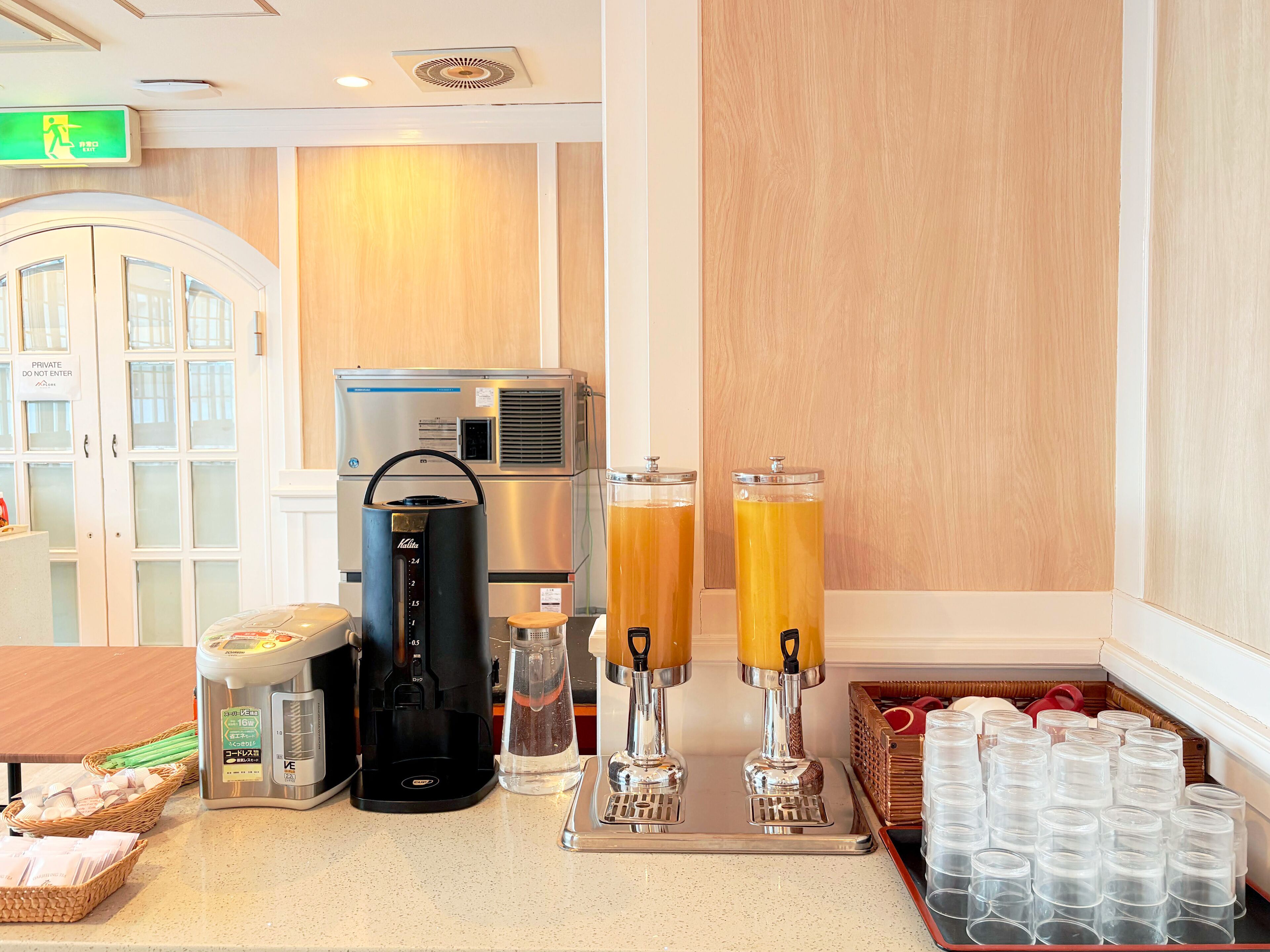 A hotel breakfast area with a coffee maker, juice dispensers, and a refrigerator.