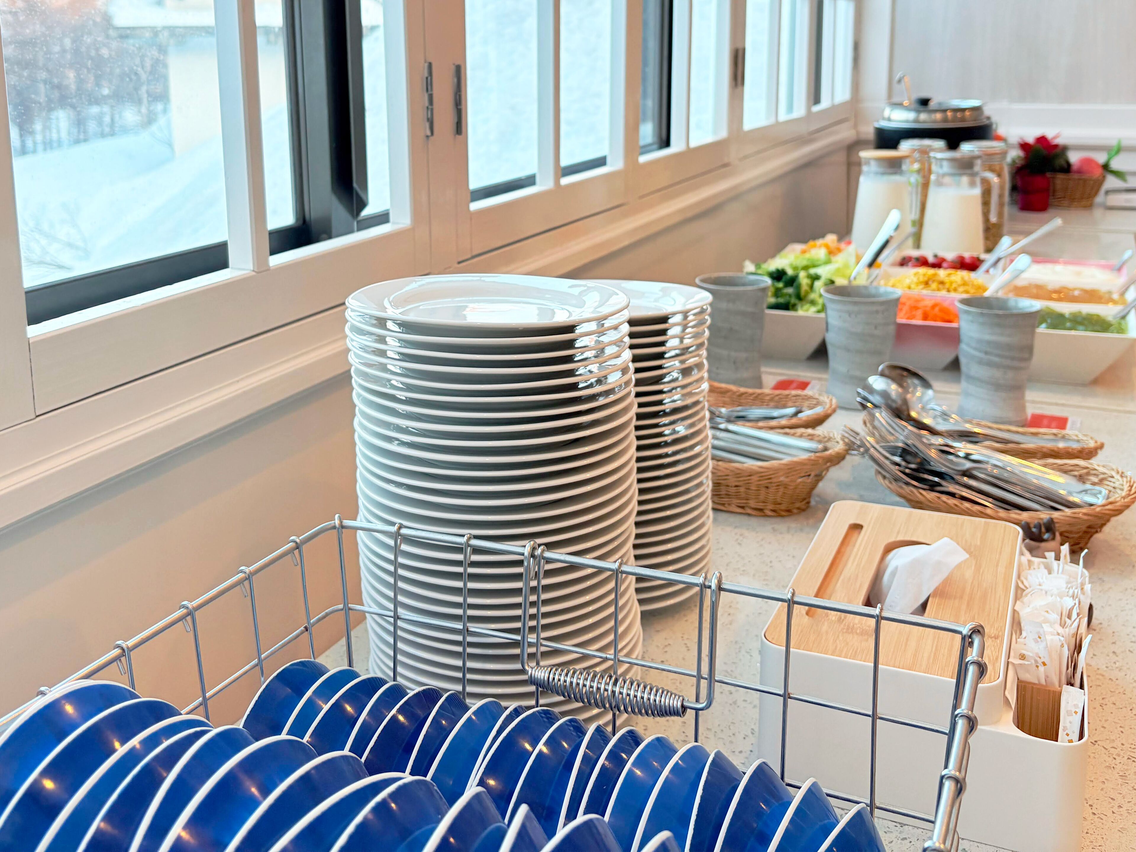 A buffet setup with stacked plates, bowls, and utensils.