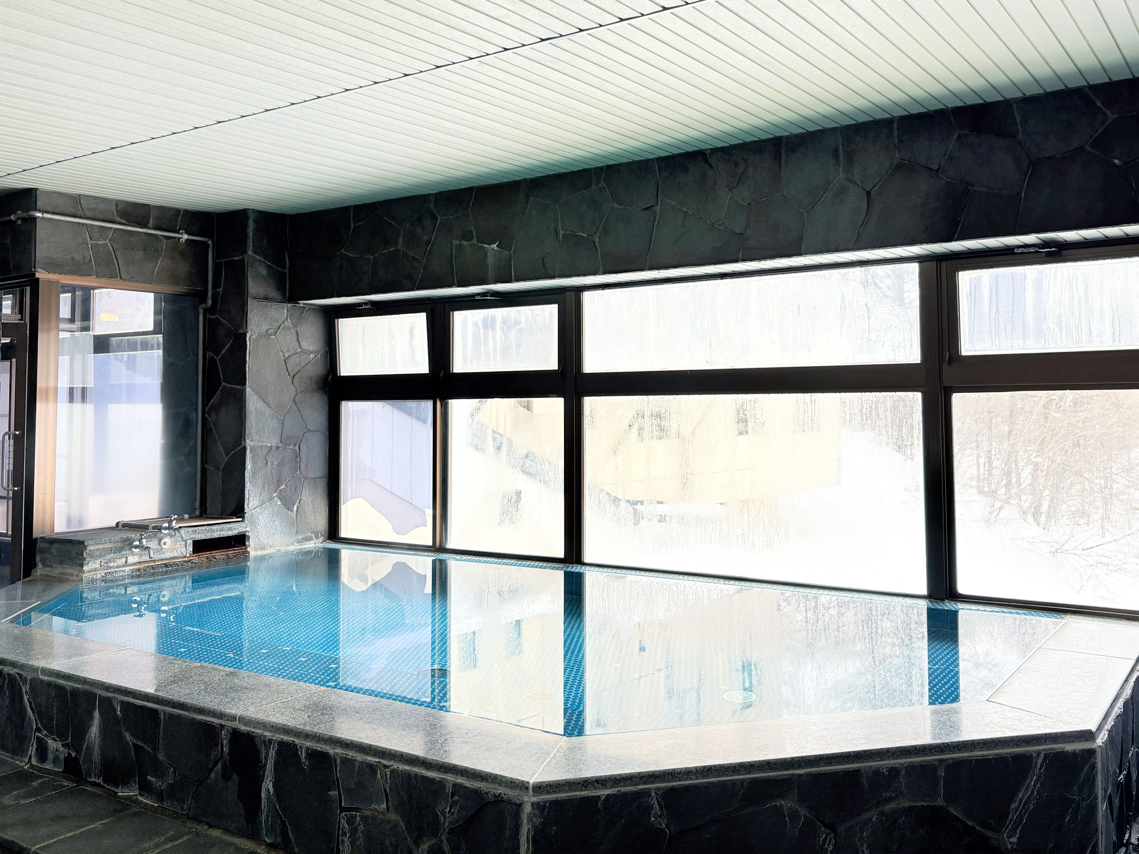 Ein Hallenbad mit Steinwänden und großen Fenstern.